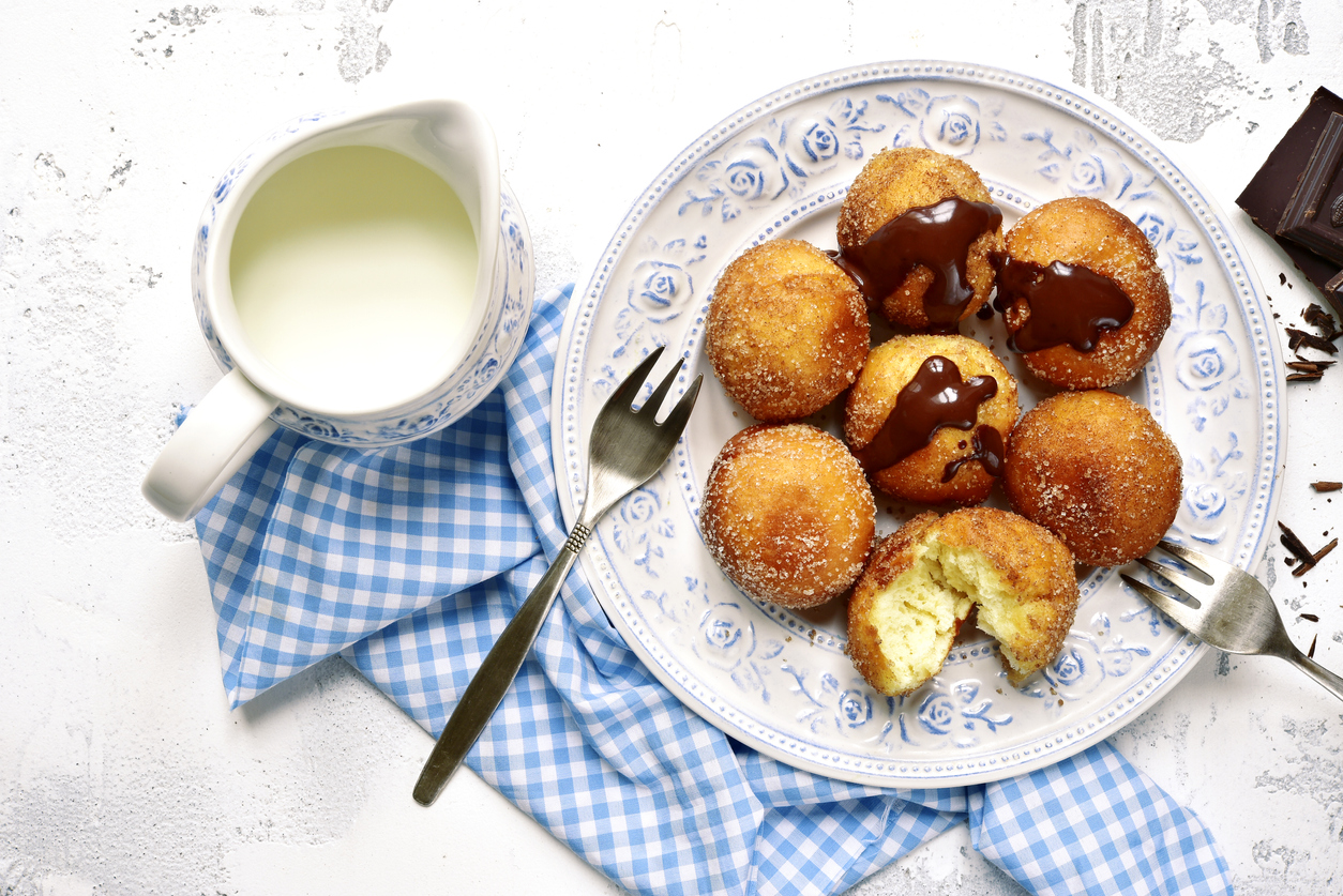 a plate of bimuelos, fried dough balls, with chocolate hazelnut spread and a pitcher of cream