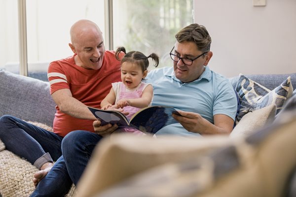 Two dads read a story to a very excited baby girl